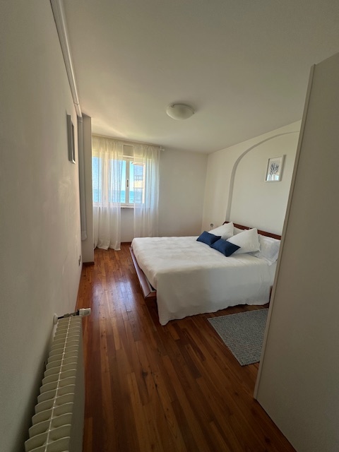 Camera da letto matrimoniale dell'appartamento di Grado con parquet, cuscini blu e finestra luminosa
